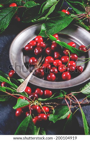 Vintage plate of fresh cherries with leaves, served with dessert fork over black