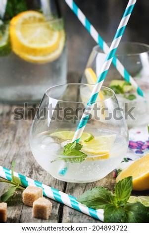 Fresh homemade lemonade with lemon, lime and mint in glasses with vintage cocktail tube over wooden table.