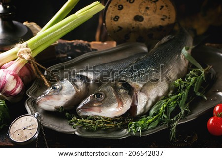 Still life with raw fish seabass, herbs, vegetables and vintage clock