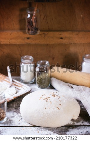 Baking bread. Dough on wooden table with flour, rolling-pin and jars with backing ingredients. See series