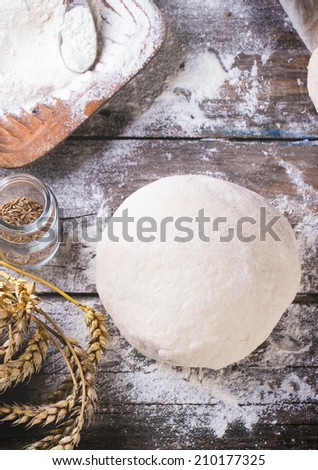 Baking bread. Dough on wooden table with flour, rolling-pin and jars with backing ingredients. Top view. See series