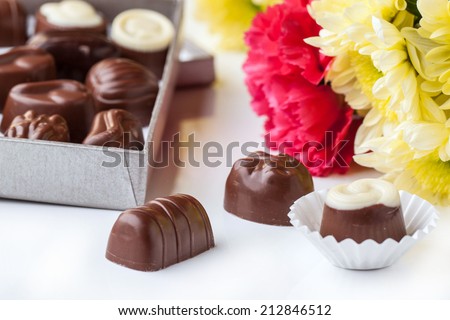 Black and white chocolate candies and bouquet of carnation and chrysanthemum flowers over white