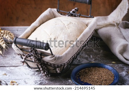Baking bread. Dough in proofing basket on wooden table with flour, cumin and wheat ears.