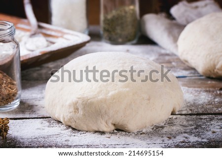 Baking bread. Dough on wooden table with flour, rolling-pin and jars with backing ingredients.