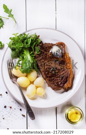 Grilled steak with butter, potatoes and green salad on white ceramic plate over white wooden table. See series