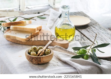 Lunch with green olives, bread and olive oil served on old wooden table near window. See series