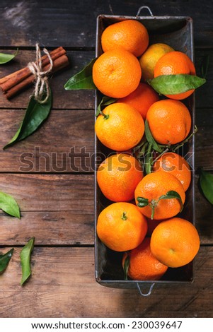 Tangerines with leaves and cinnamon stick on old wooden table. Top view.