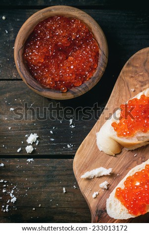 Bowl and sandwiches with red caviar served on olive wood cutting board over old wooden table. Top view. See series