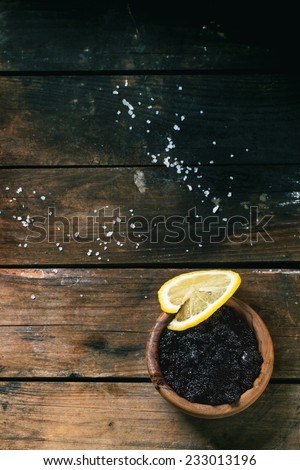 Wooden bowl of black caviar with lemon slice over old wooden table. Top view.
