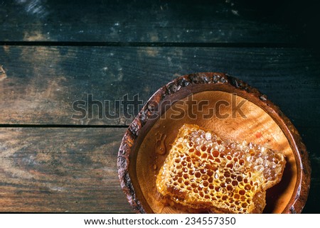 Honeycomb in wooden bowl over old wooden table. Top view.