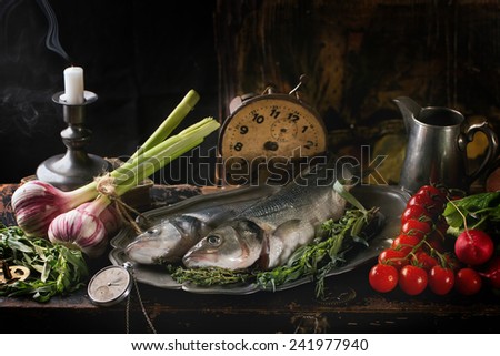 Still life with raw fish seabass, herbs, vegetables and vintage clock