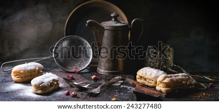 Tea drinking with eclairs and chopped chocolate, served with vintage teapot and cutlery over dark background. See series