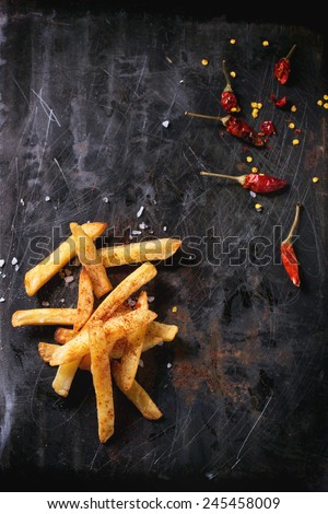 Fried potatoes with sea salt and red hot chili pepper over black metal surface