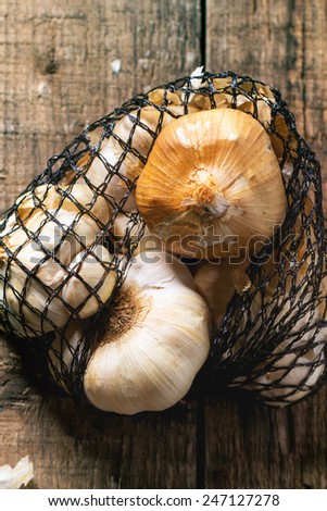 Mesh bag of smoked garlic over wooden background. Top view. See series