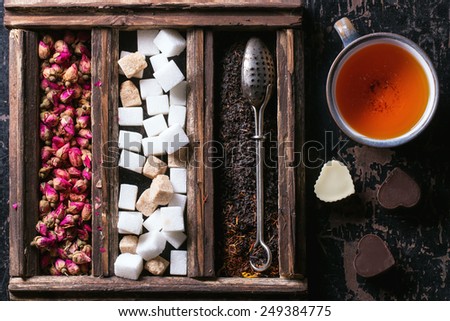 Set of dry black tea, tea roses and sugar cubes in wooden box with vintage tea strainer and cup of tea