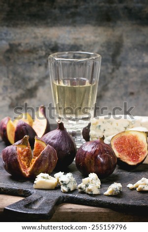 Figs with blue cheese, white wine and crackers on black cutting board. See series.