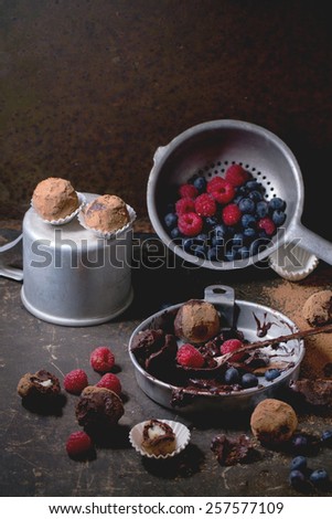 Aluminium plate with chocolate mixture for making chocolate truffles and homemade chocolate truffles with fresh berries over dark table.