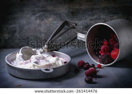 Aluminium plate with homemade vanilla ice cream and mix of frozen berries, served with metal spoon over metal table. See series