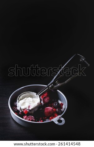 Aluminium plate with homemade vanilla ice cream and mix of frozen berries, served with metal spoon over black table