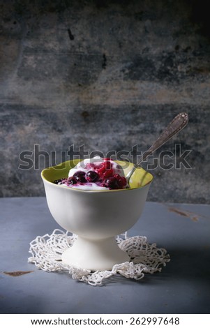 White ceramic vase with homemade vanilla ice cream, served with mix of berries over gray metal table