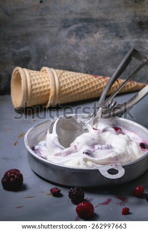 Aluminium plate with homemade vanilla ice cream, mix of frozen berries and waffer cones, served with metal spoon over metal table. See series