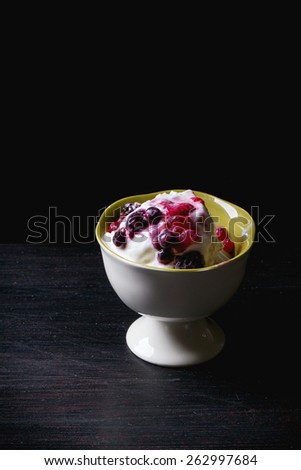 White ceramic vase with homemade vanilla ice cream, served with mix of berries over dark table
