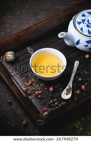 Traditional japanese teapot and cup of green tea, served on bamboo tray with dry tea variations over dark background