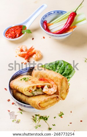 Fried spring rolls with vegetables and shrimps, served with spicy sauce over white wooden background.
