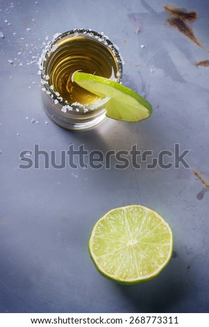 Short of tequila anejo with lime and salt over gray metal table. Overhead view.