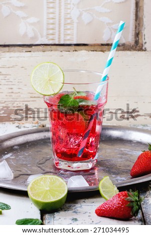 Glass with retro cocktail tubes with homemade strawberry lemonade, served with fresh strawberries, mint, lime and ice cubes over old white wooden table. See series