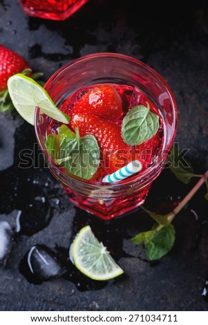 Glass with retro cocktail tubes with homemade strawberry lemonade, served with fresh strawberries, mint, lime and ice cubes overdark background. See series