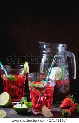 Two glasses with retro coctail tubes and glass jug of strawberry lemonade, served with fresh strawberries, mint and  lime over dark background. See series