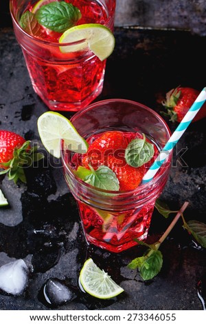 Two glasses with retro cocktail tubes with homemade strawberry lemonade, served with fresh strawberries, mint, lime and ice cubes overdark background. See series