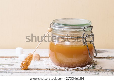 Jar of homemade caramel sauce, served with sugar cubes over wooden table