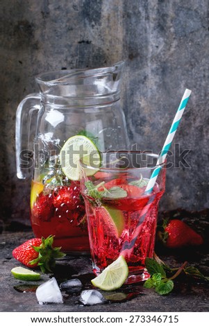 Glass with retro coctail tubes and glass jug of strawberry lemonade, served with fresh strawberries, mint and  lime over dark background. See series