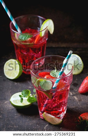 Two glasses with retro cocktail tubes with homemade strawberry lemonade, served with fresh strawberries, mint, lime and ice cubes overdark background. See series
