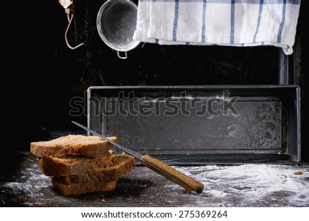 Sliced homemade rye bread over kitchen table powdered with flour, with towel, bread pan and vintage stainer and steelyard at background