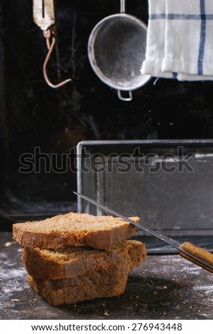 SliÃ?Â�ed homemade rye bread over kitchen table powdered with flour, with towel, bread pan and vintage stainer and steelyard at background.