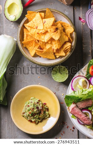 Overhead view on mexican style dinner with tacos, vegetables, nachos chips and guakomole, served over gray wooden table