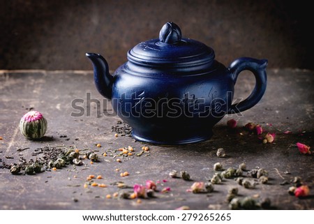Blue ceramic teapot served with black and green tea lives over dark background