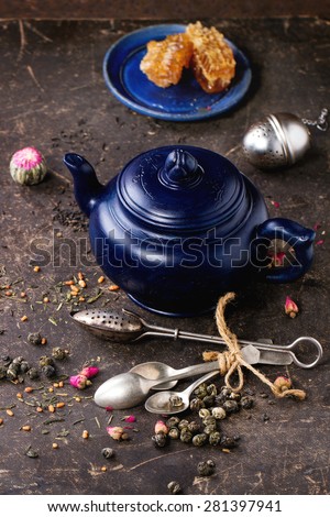 Blue ceramic teapot and plate with honeycombs, served with spoons, black and green tea lives over dark background