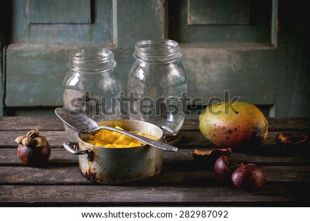 Making mango chutney or jam in vintage aluminum pan over old table with empty glass jar, mango and mangosteen. Dark rustic atmosphere