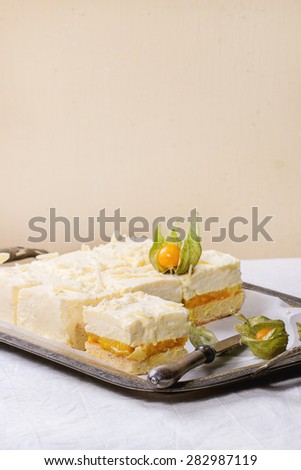 Homemade sliced cake with creamy mousse and tropical fruits mango and physalis served in vintage metal tray over white table