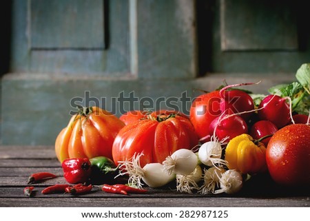 Heap of fresh ripe colorful vegetables tomatoes, chili peppers, green onion and bunch of radish over old wooden table. Dark rustic atmosphere