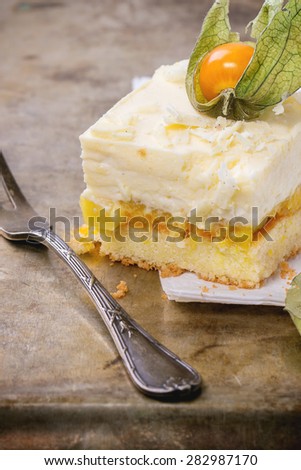 Piece of homemade sliced cake with creamy mousse and tropical fruits mango and physalis over metal background with vintage fork