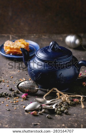 Blue ceramic teapot and plate with honeycombs, served with spoons, black and green tea lives over dark background. Chinese inscription on teapot - traditional tea drinking