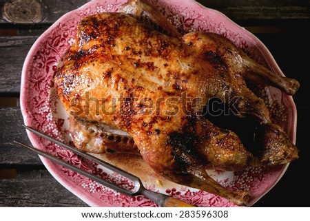 Whole roast honey duck with meat fork in vintage plate, served over old wooden table. Top view