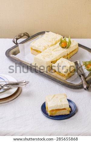 Homemade sliced cake with creamy mousse and tropical fruits mango and physalis served in vintage metal tray over white table. Selective focus