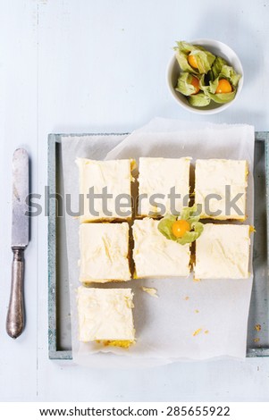 Homemade sliced cake with creamy mousse and tropical fruits mango and physalis served in wooden tray over light blue background. Top view