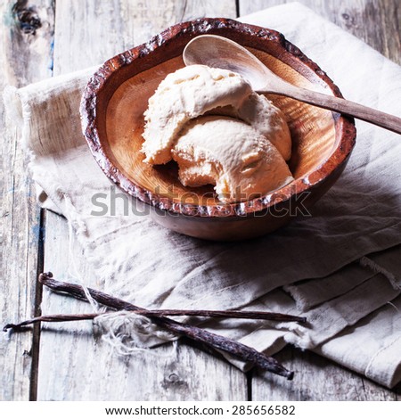 Wooden bowl with vanilla ice cream and vanilla stick on old wooden table. Square image, selective focus